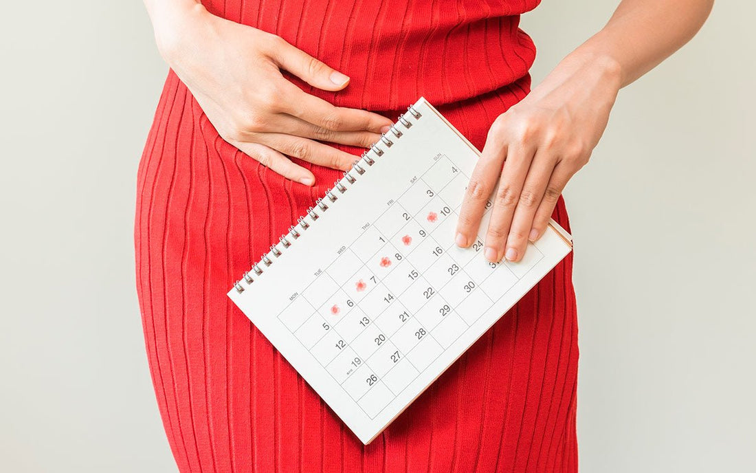 Person hält sich ihren Bauch und hält einen Zykluskalender in der anderen Hand
